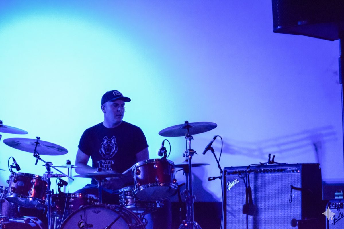 Ethan Wright playing drums in the background during a live set